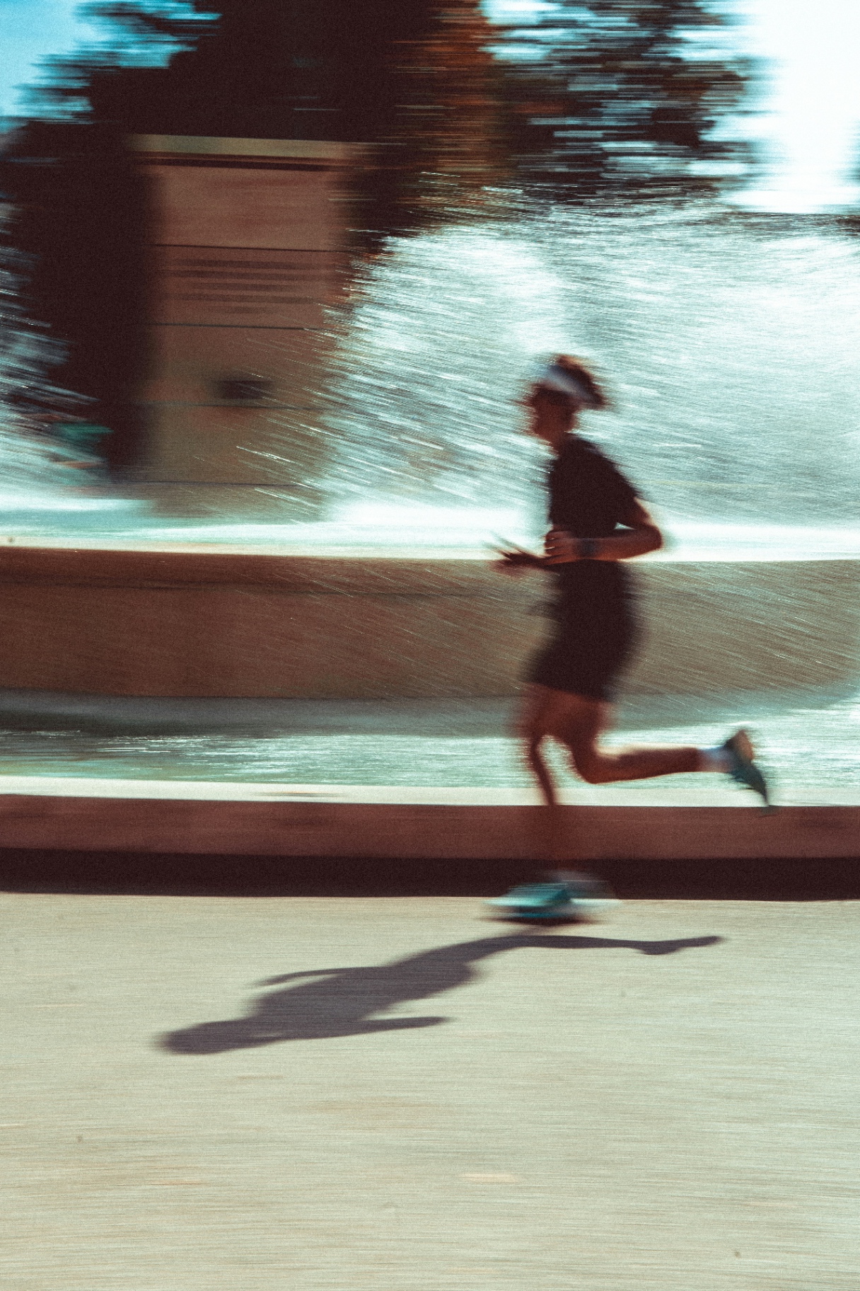 A runner in motion past a sunlit fountain